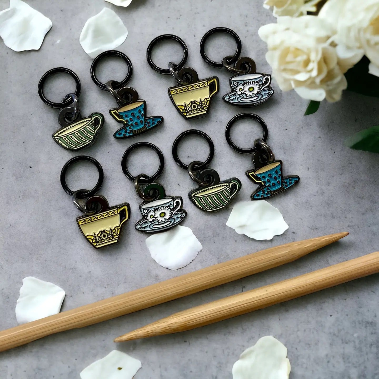 Tea cup keychains on a gray surface with wooden sticks and flowers.