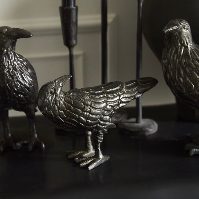 Three metallic bird figurines on a dark surface with a blurred background
