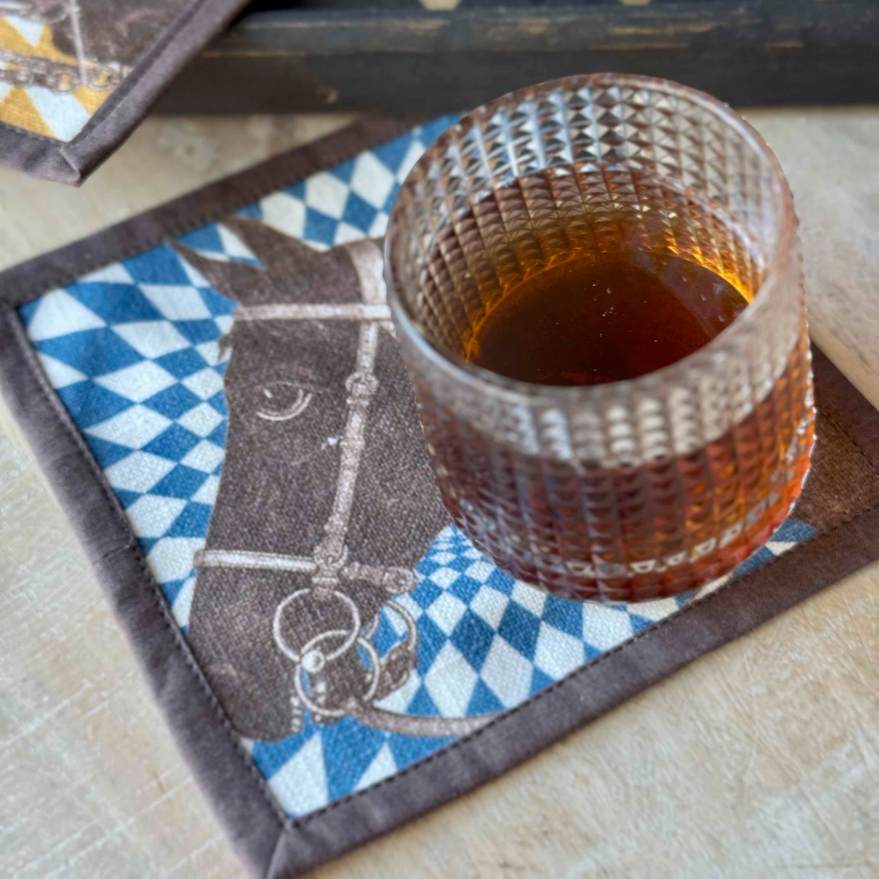 Glass of amber liquid on a decorative coaster with a horse design