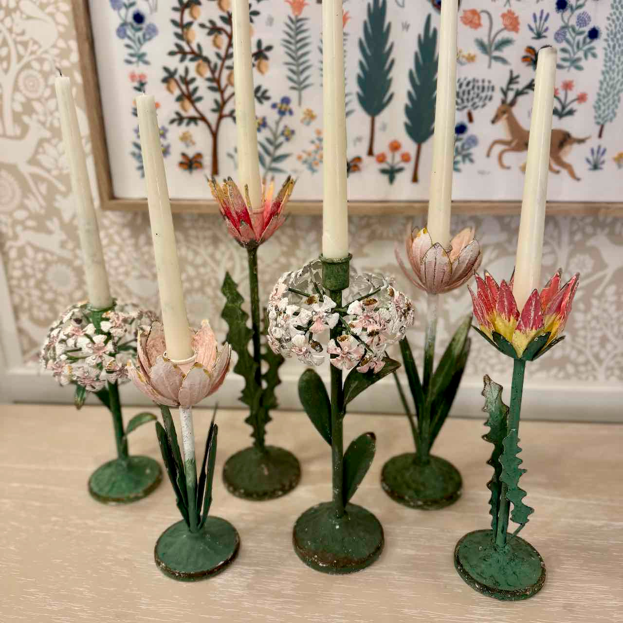Decorative candle holders shaped like flowers on a wooden surface with a floral-patterned wall in the background.