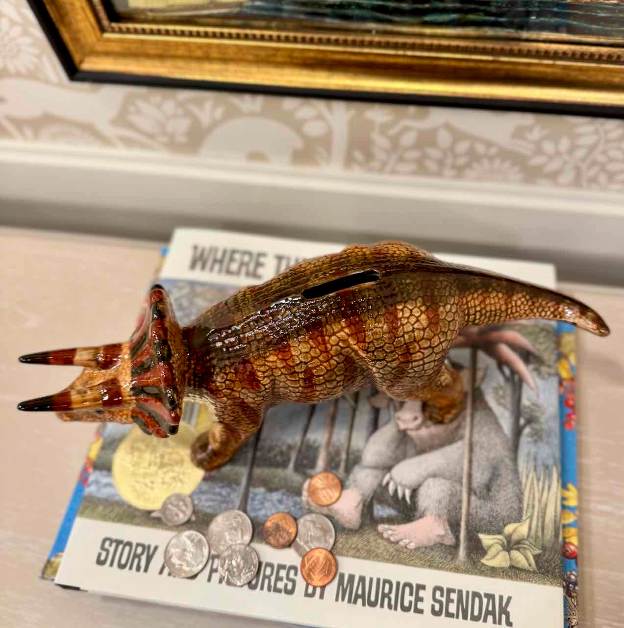 Dinosaur toy on top of a book with a gold frame in the background