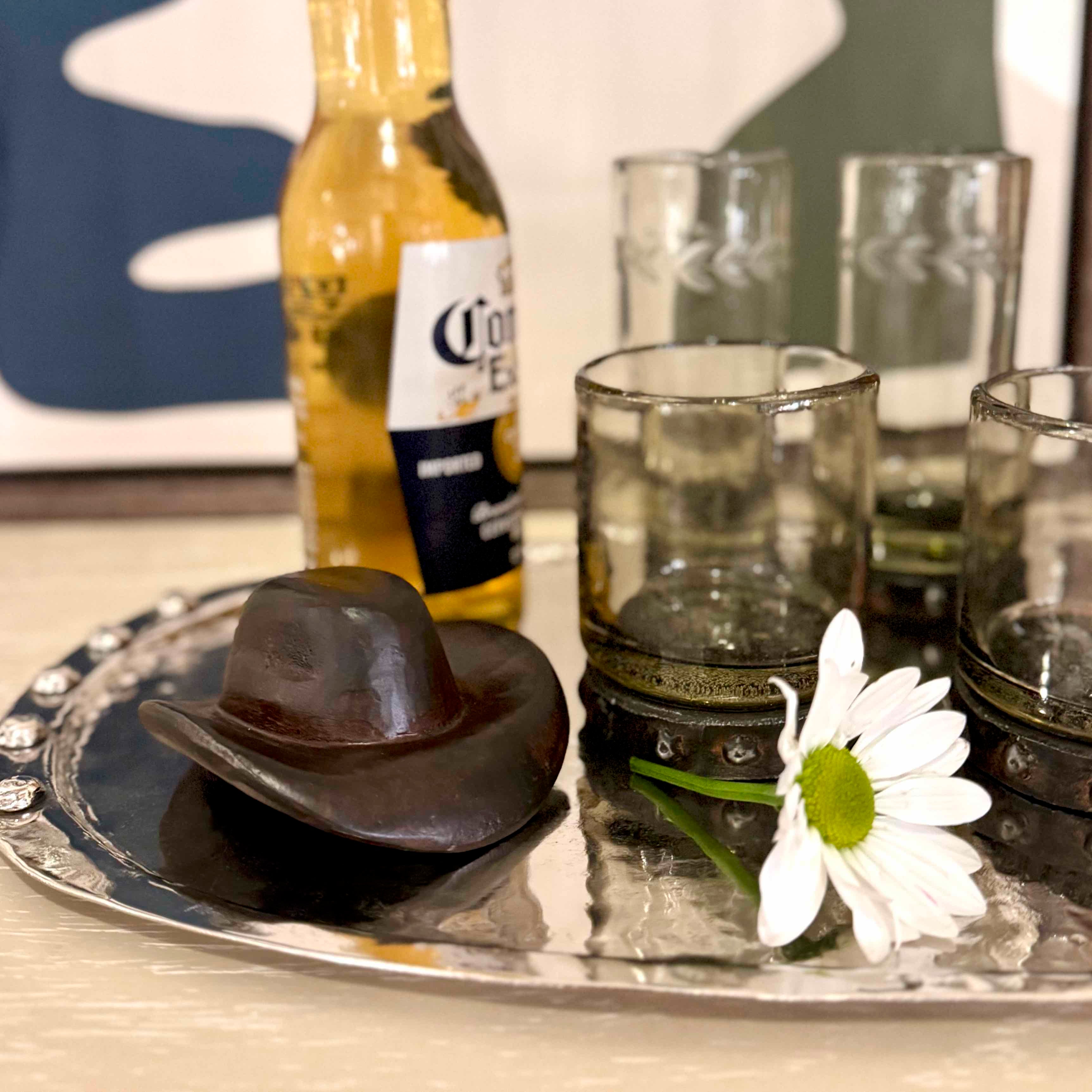 Tray with a cowboy hat, daisy, and Corona beer bottle on a reflective surface.