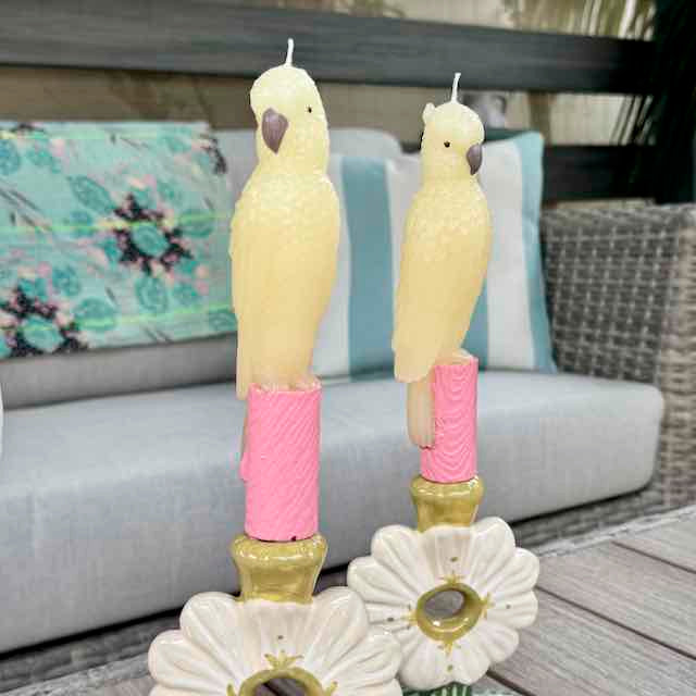 Two parrot-shaped candles with pink bases on a decorative stand outdoors.