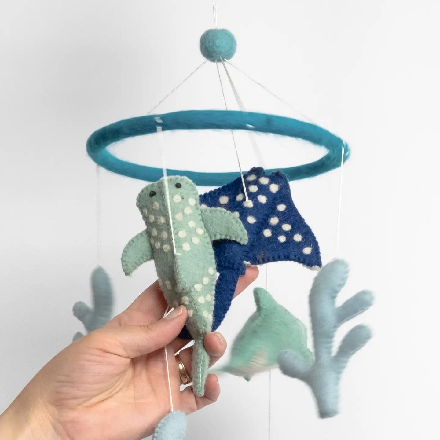 Handmade plush whale and starfish mobile held by a hand against a white background