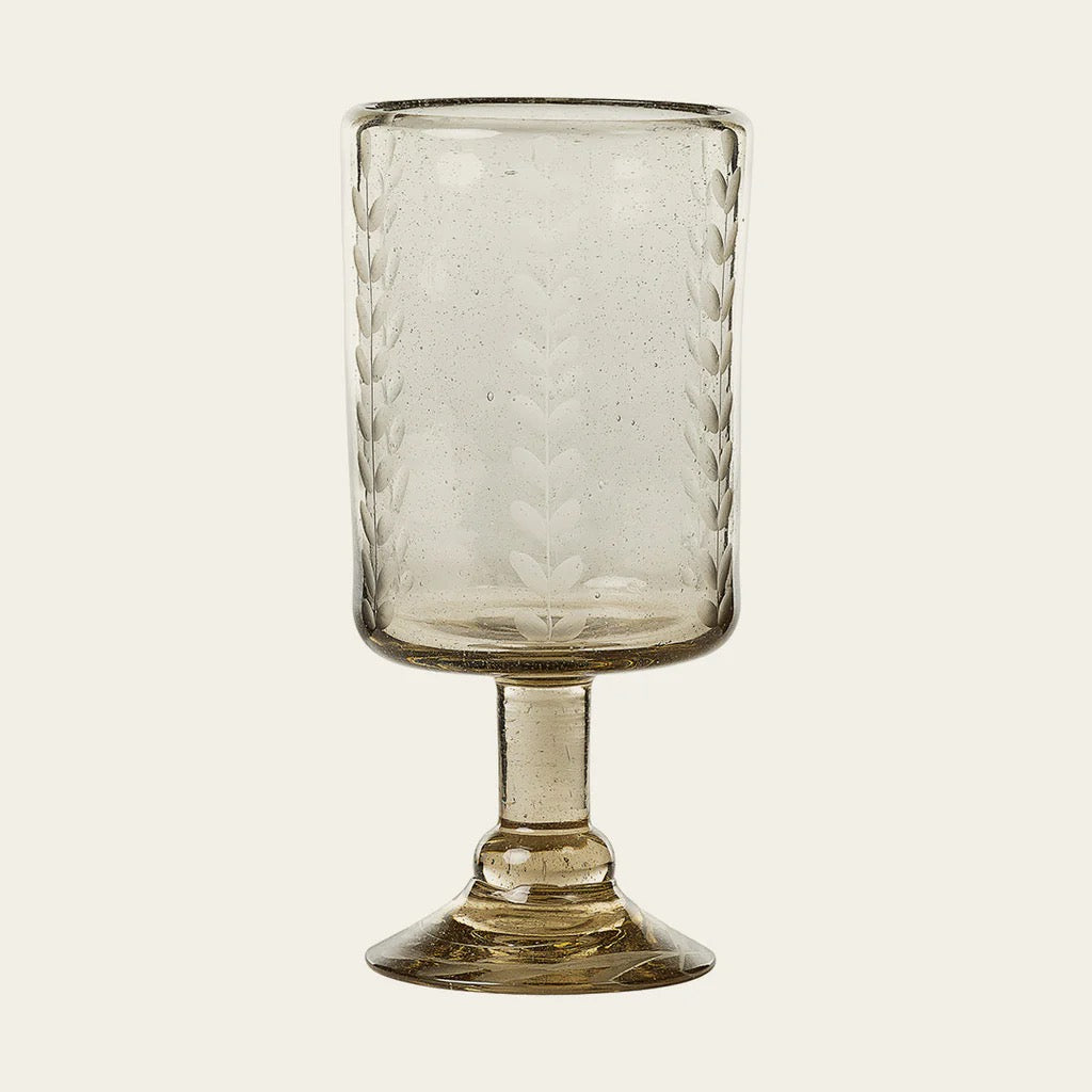 A clear glass with vertical etched laurel leaves design on it, standing on a solid base.