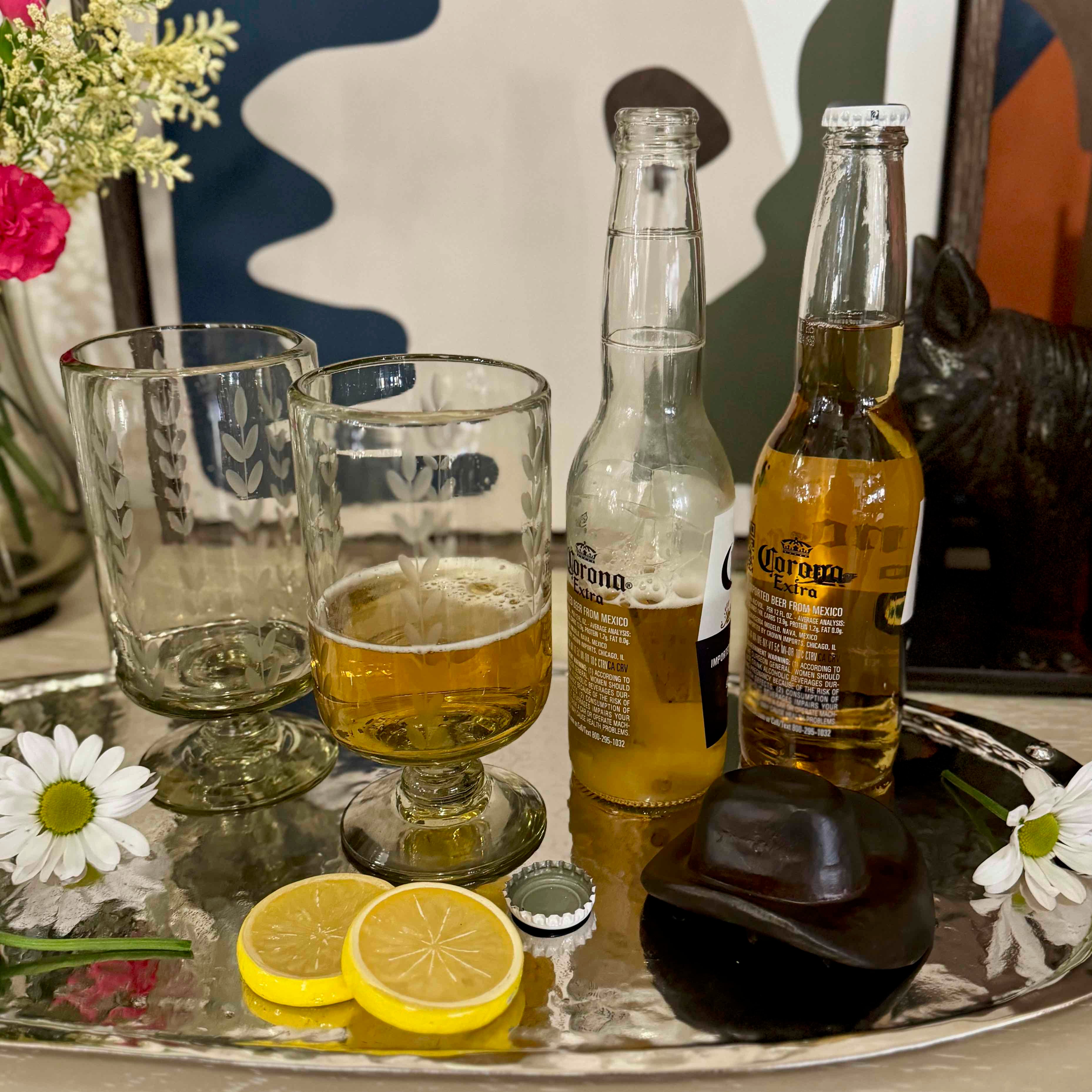 Two bottles of Corona beer with glasses and lemon slices on a tray.