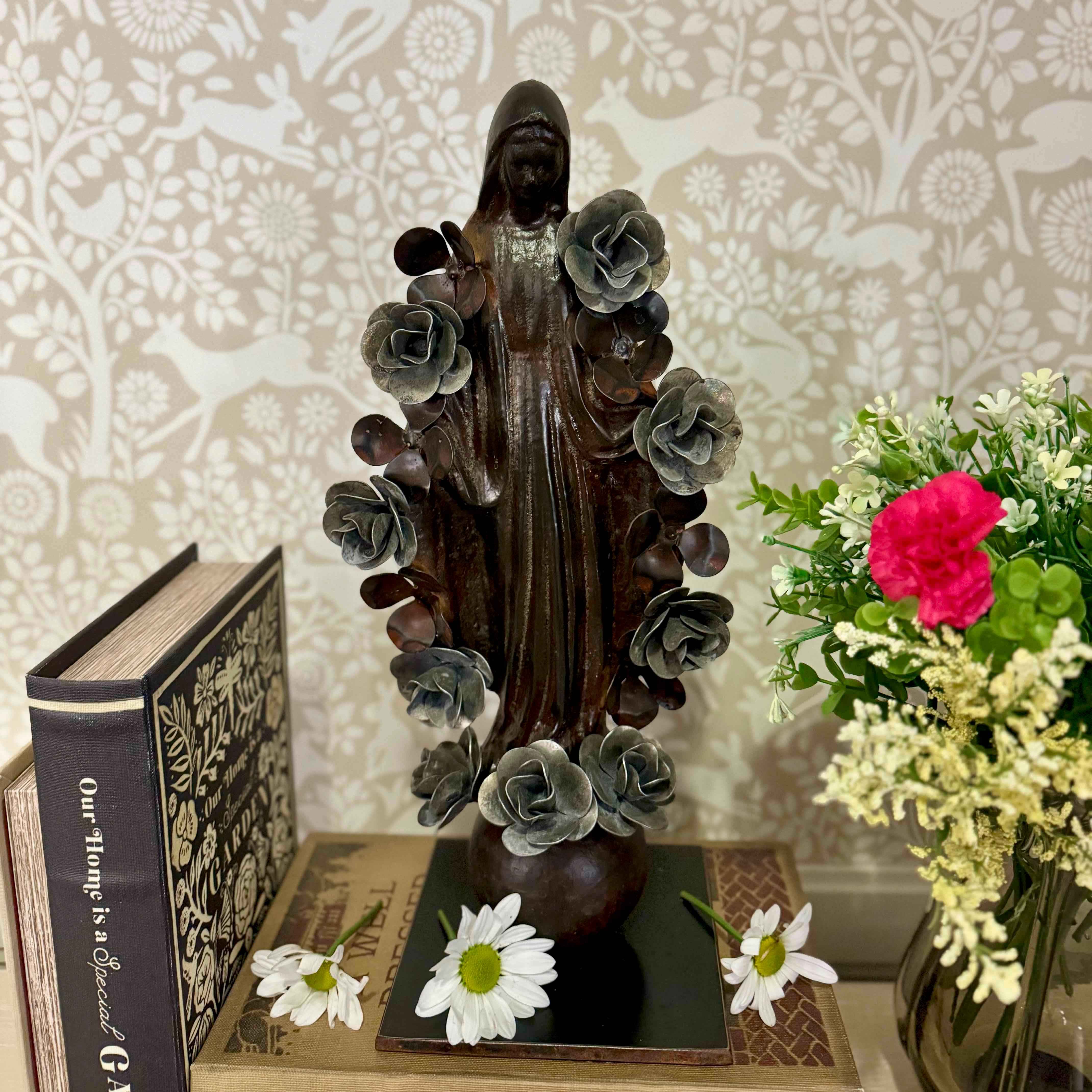 Statue of a religious figure with floral elements on a table with books and flowers.