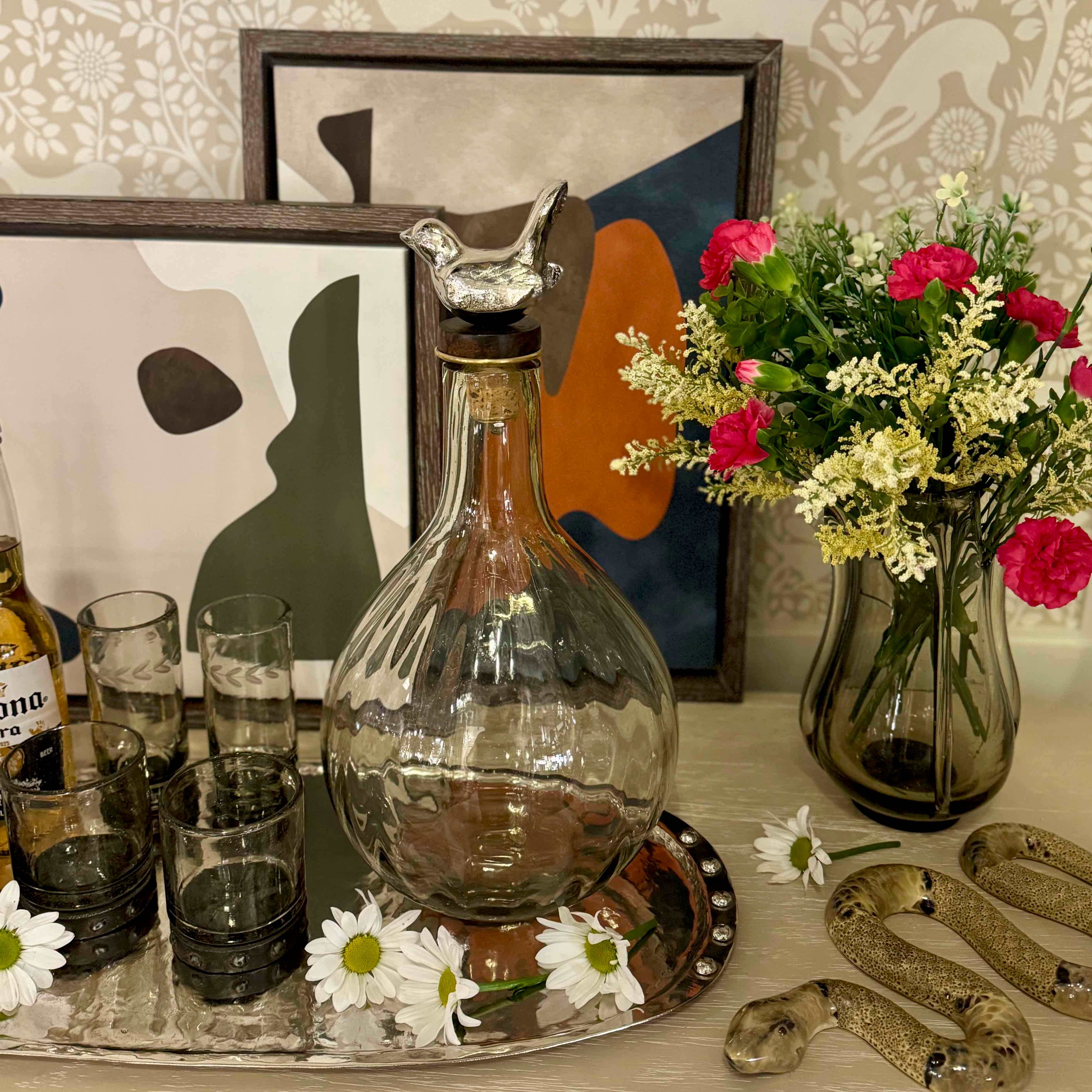 Decorative setting with a glass decanter, flowers, and framed art on a table.