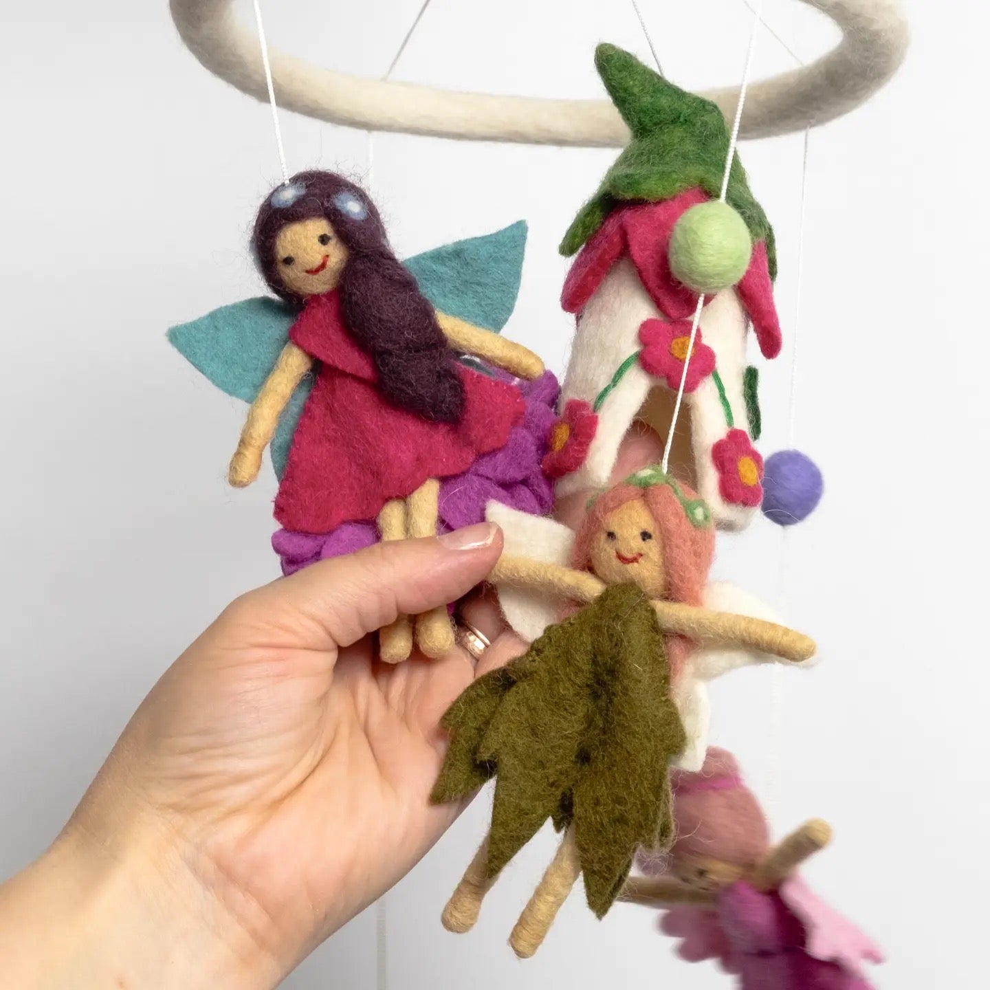 Handmade fairy dolls hanging from a circular wooden frame against a white background