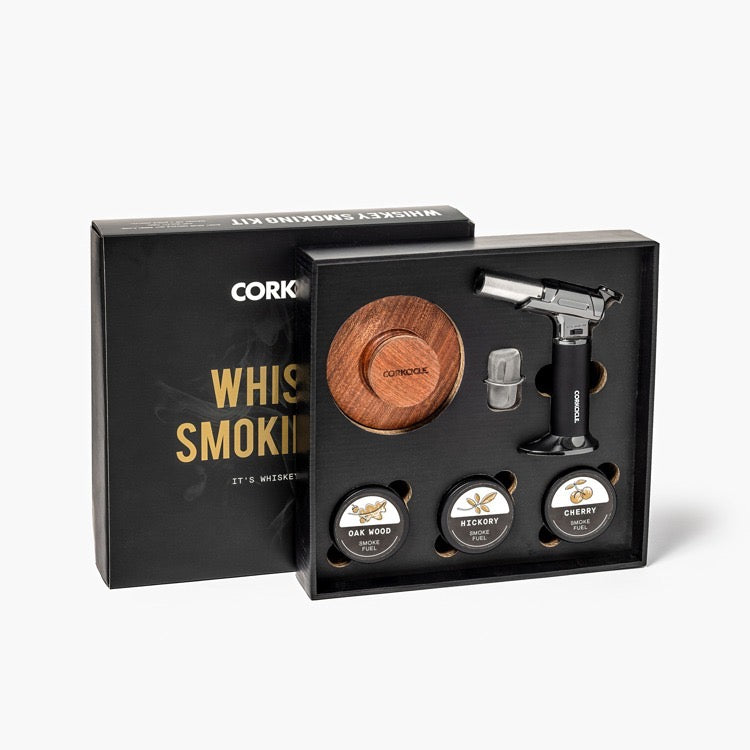 Whiskey smoking kit with wooden disc, metal tool, and labeled stones in a black box.
