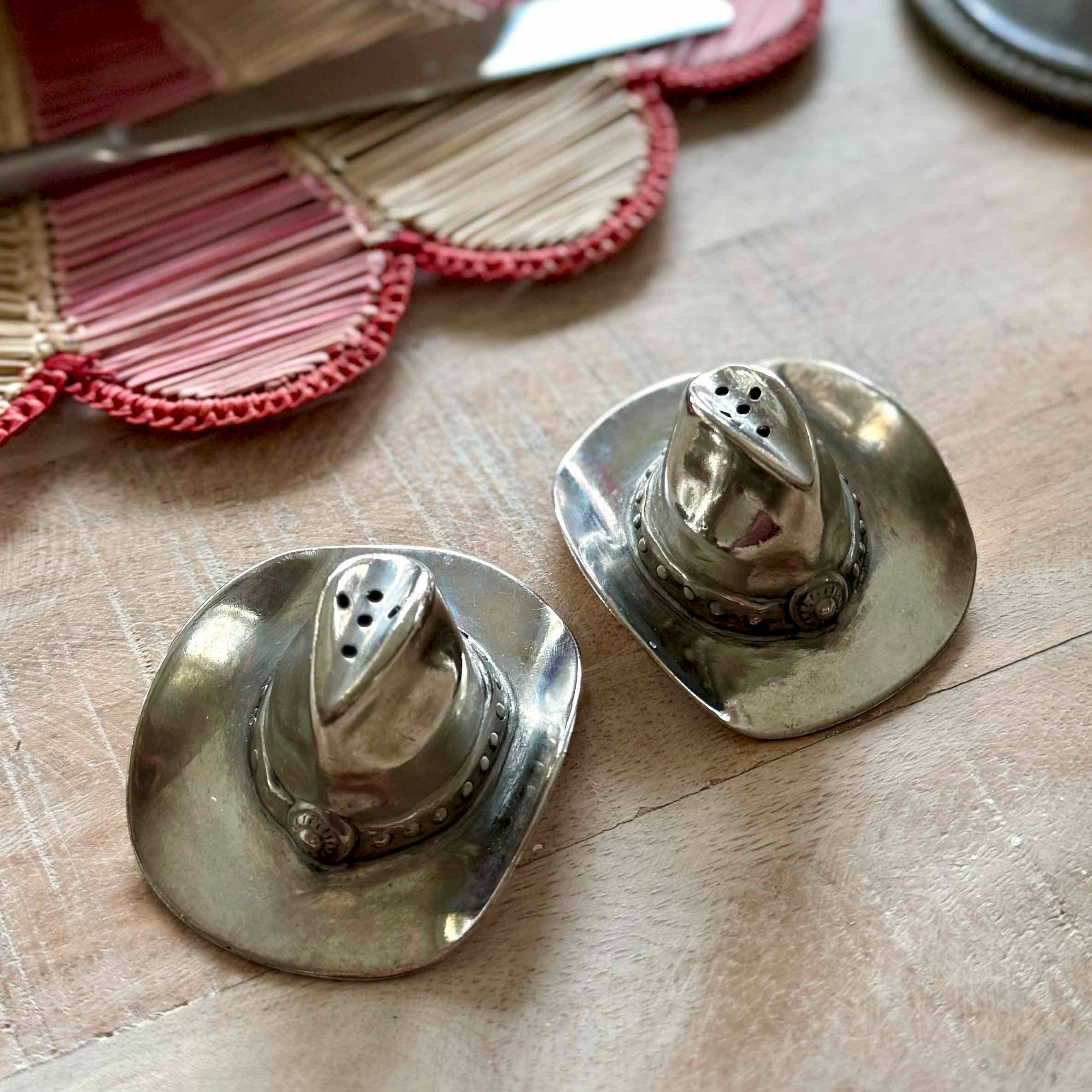 Silver cowboy hat-shaped salt and pepper shakers on a wooden surface.