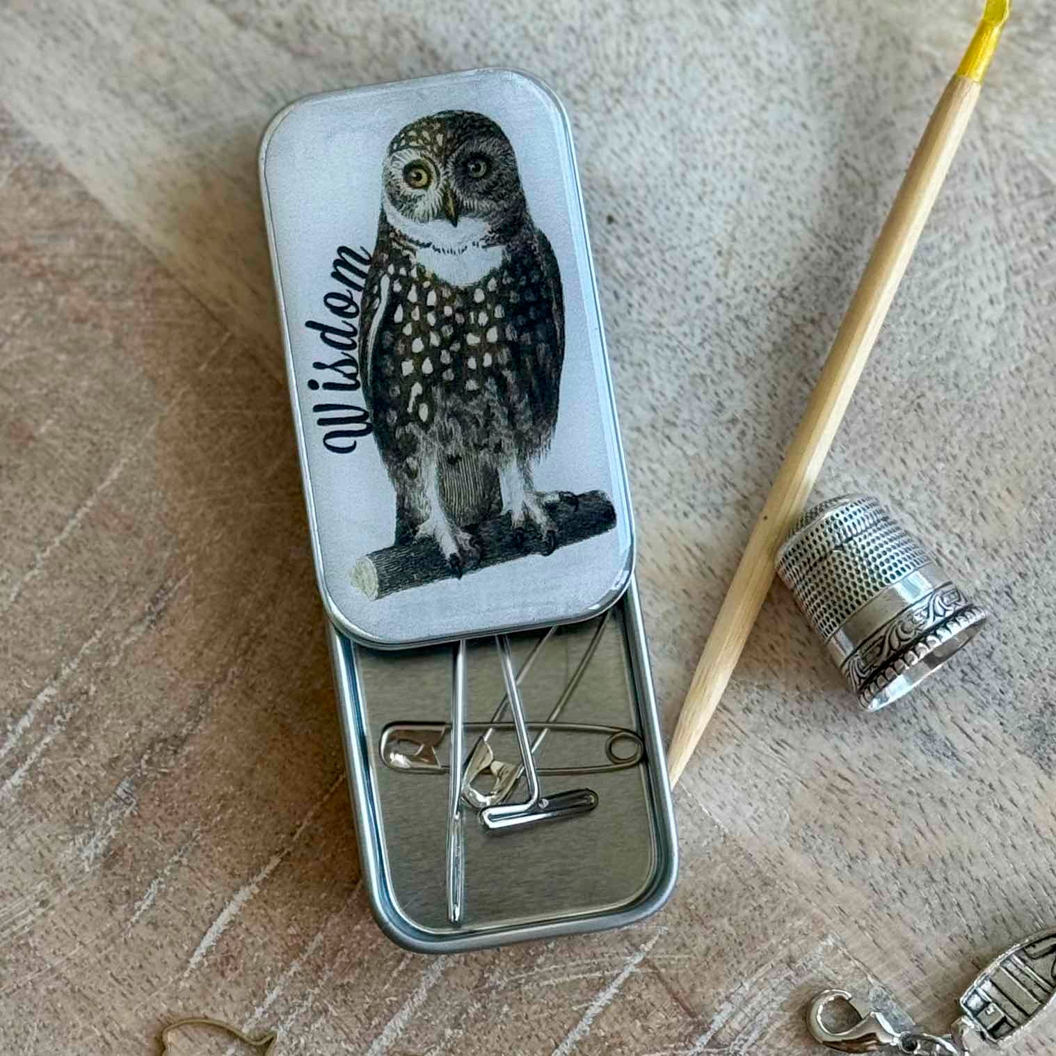 Small tin with owl design and sewing tools on a textured surface