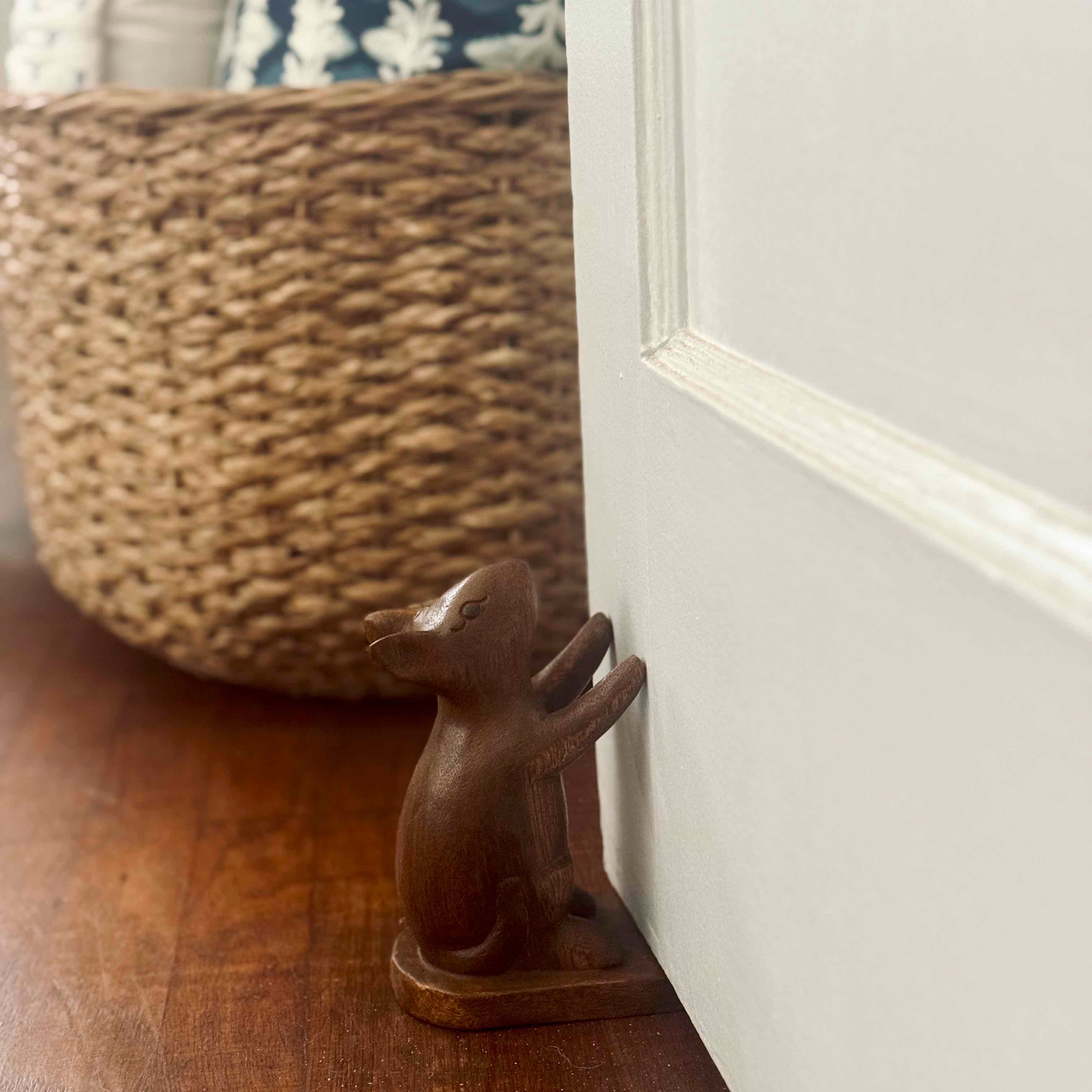 Wooden rabbit-shaped doormat holder on a wooden floor next to a white door.