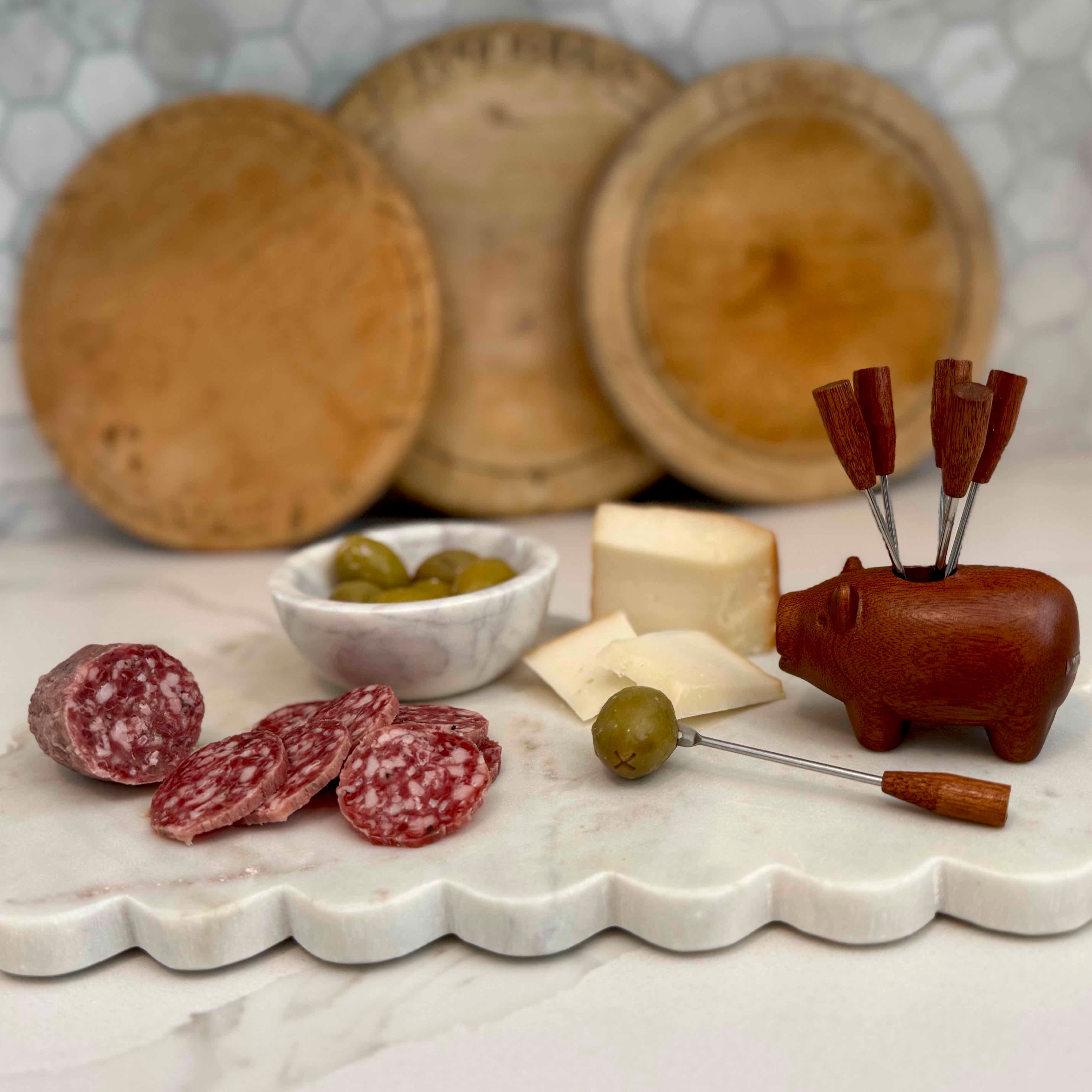 Wooden charcuterie board with cured meats, olives, and a cheese block on a marble surface.