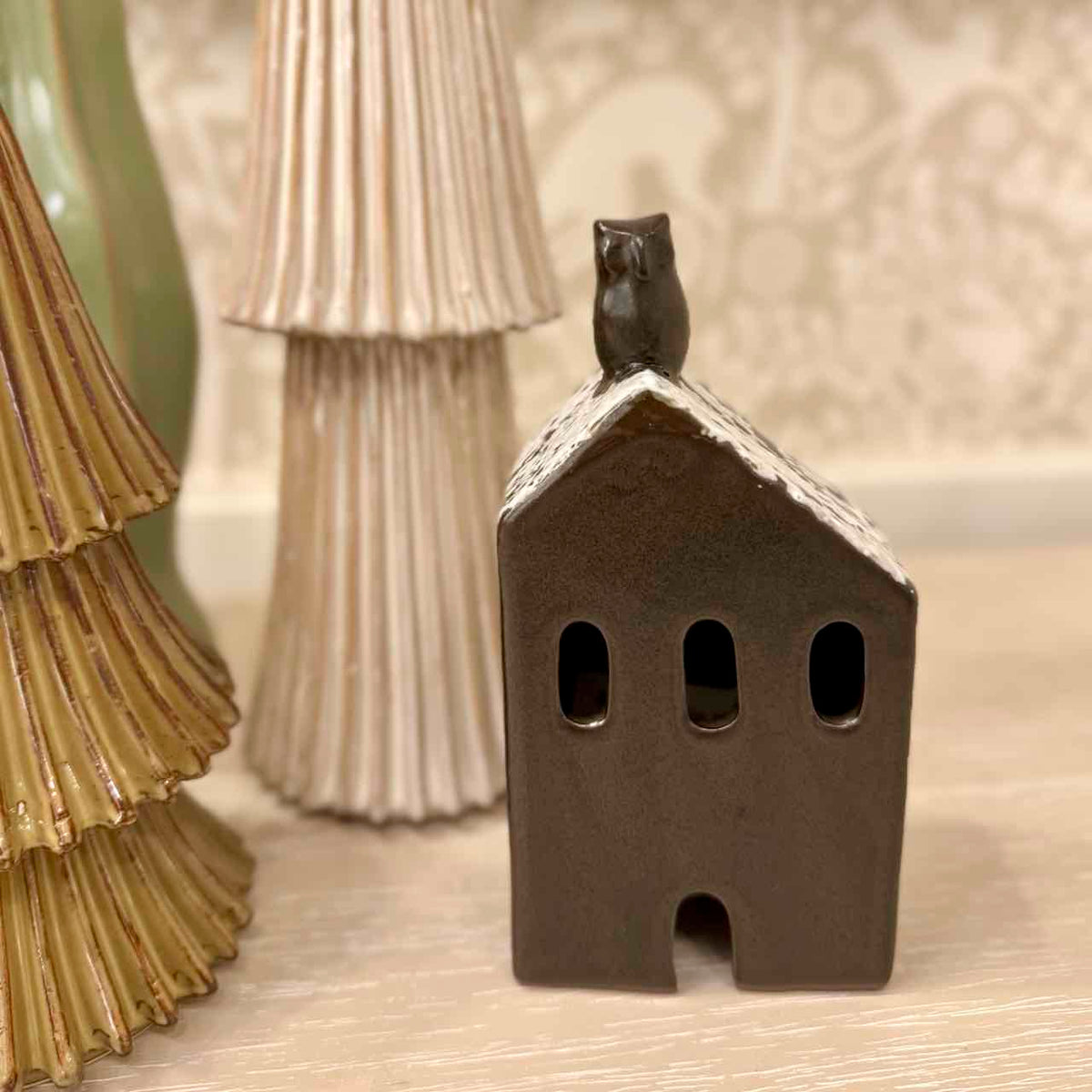 Small ceramic house with a cat figurine on top, placed on a textured surface.