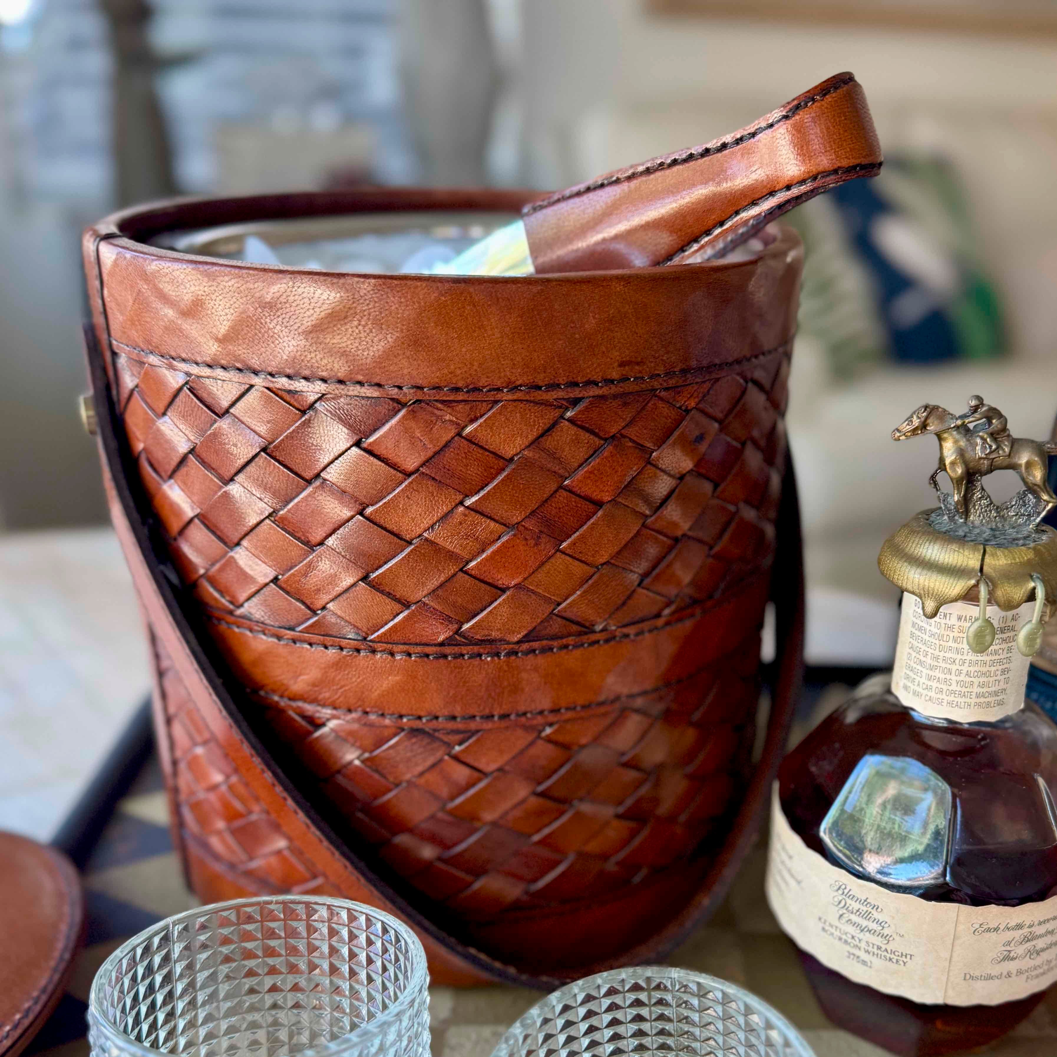 Brown woven leather bag next to a bottle with a decorative cap on a table.