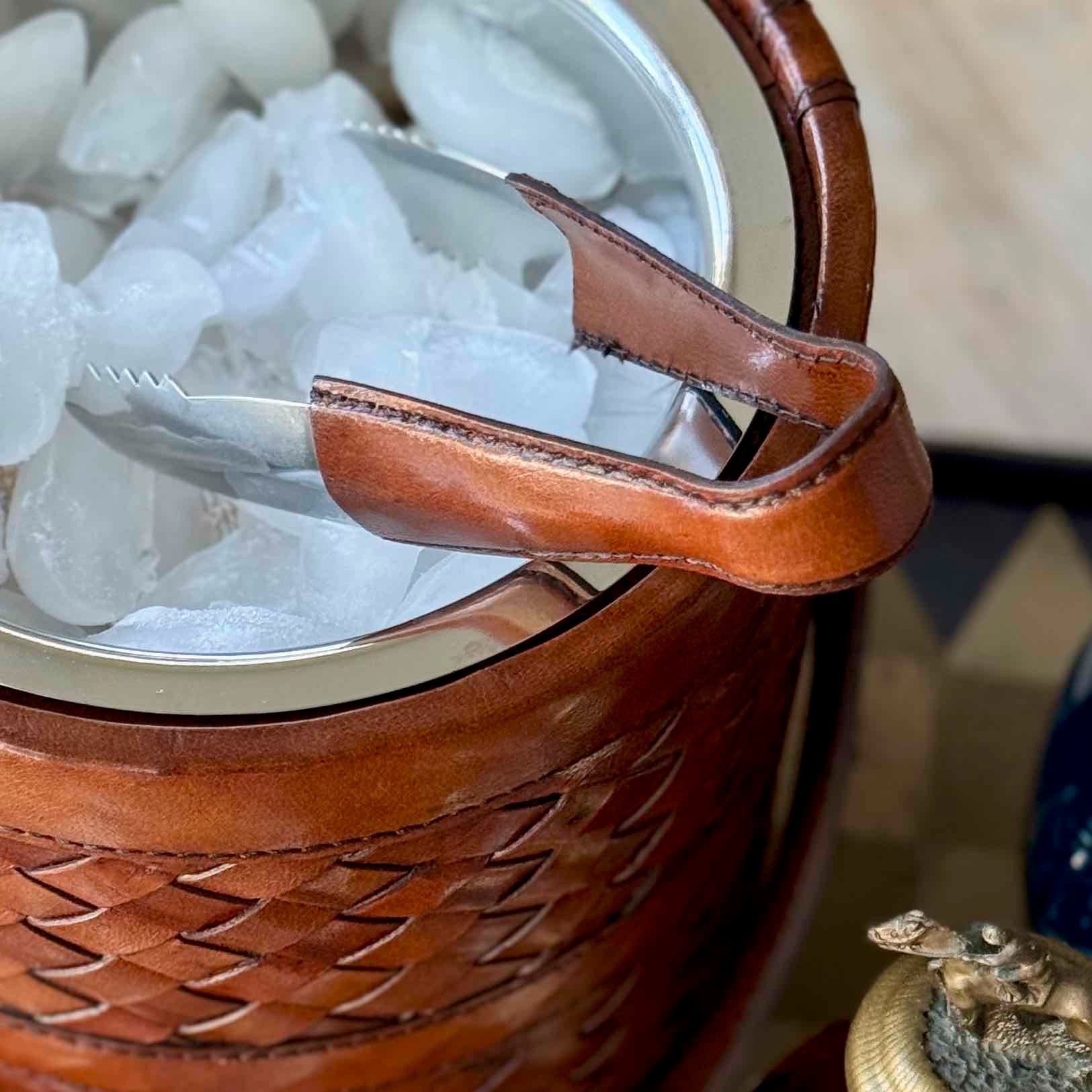 Brown woven ice bucket with leather handle and ice cubes inside