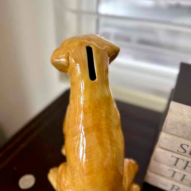 Brown ceramic dog figurine with a coin slot on a blurred background