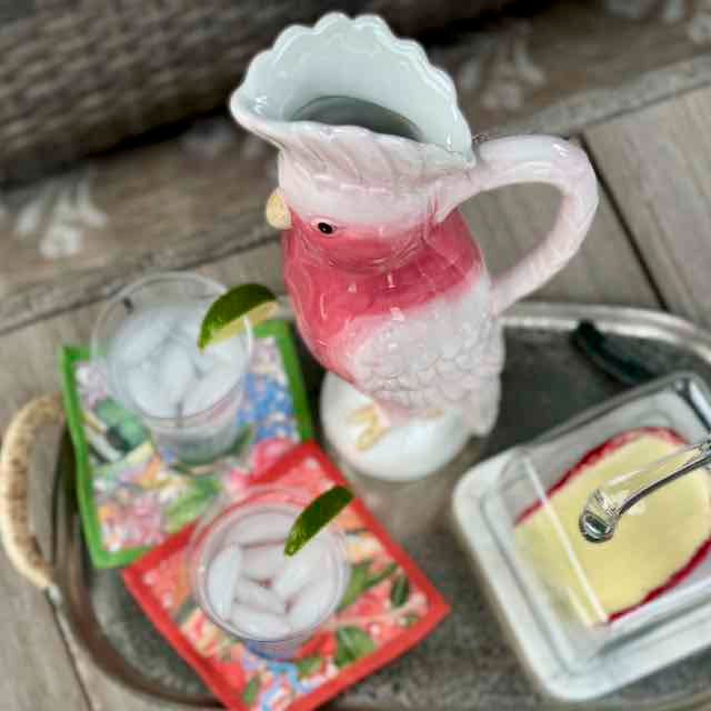 Decorative pitcher with a pink interior on a table with glasses and a dish.