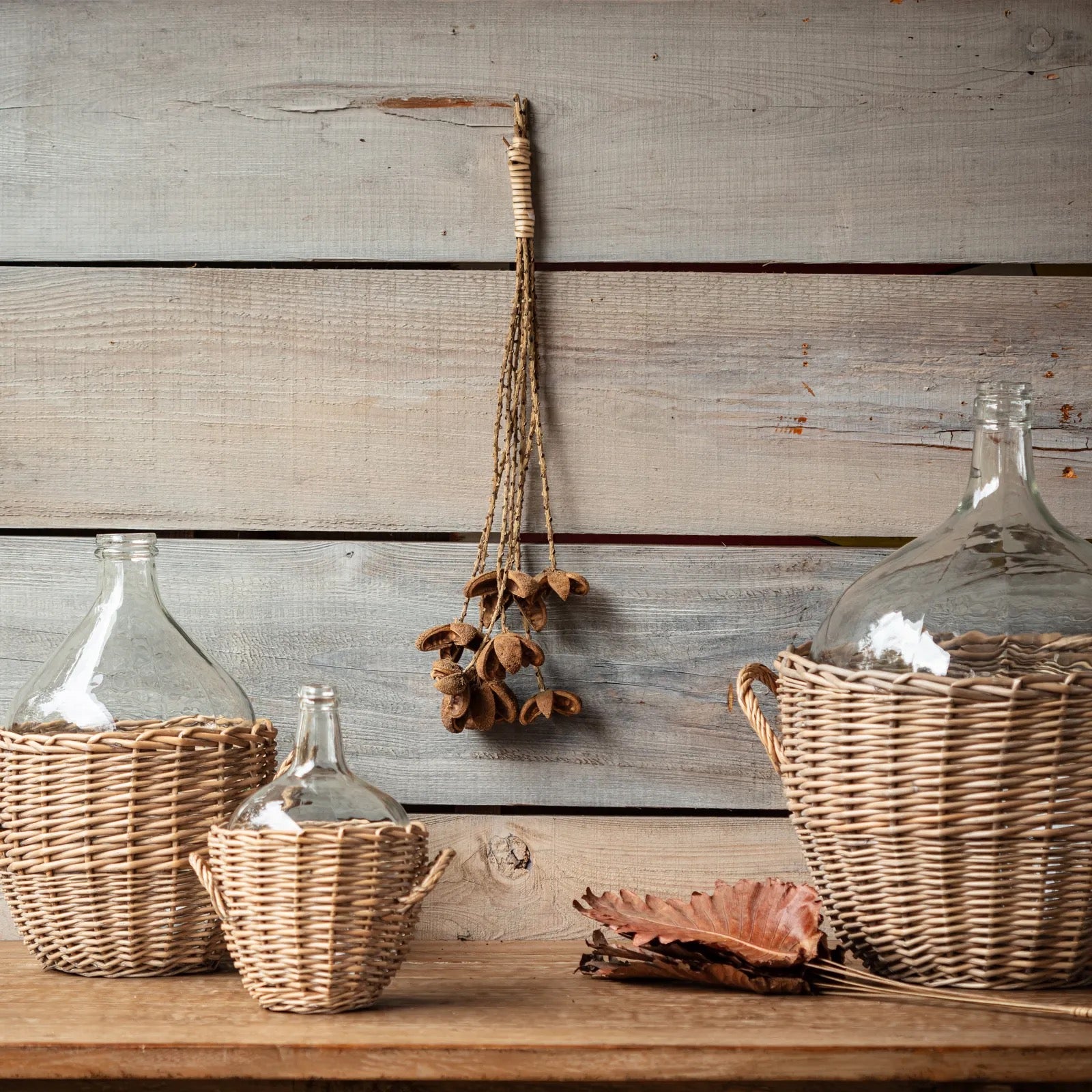 Decorative glass jars with wicker baskets on a wooden surface against a wooden wall.