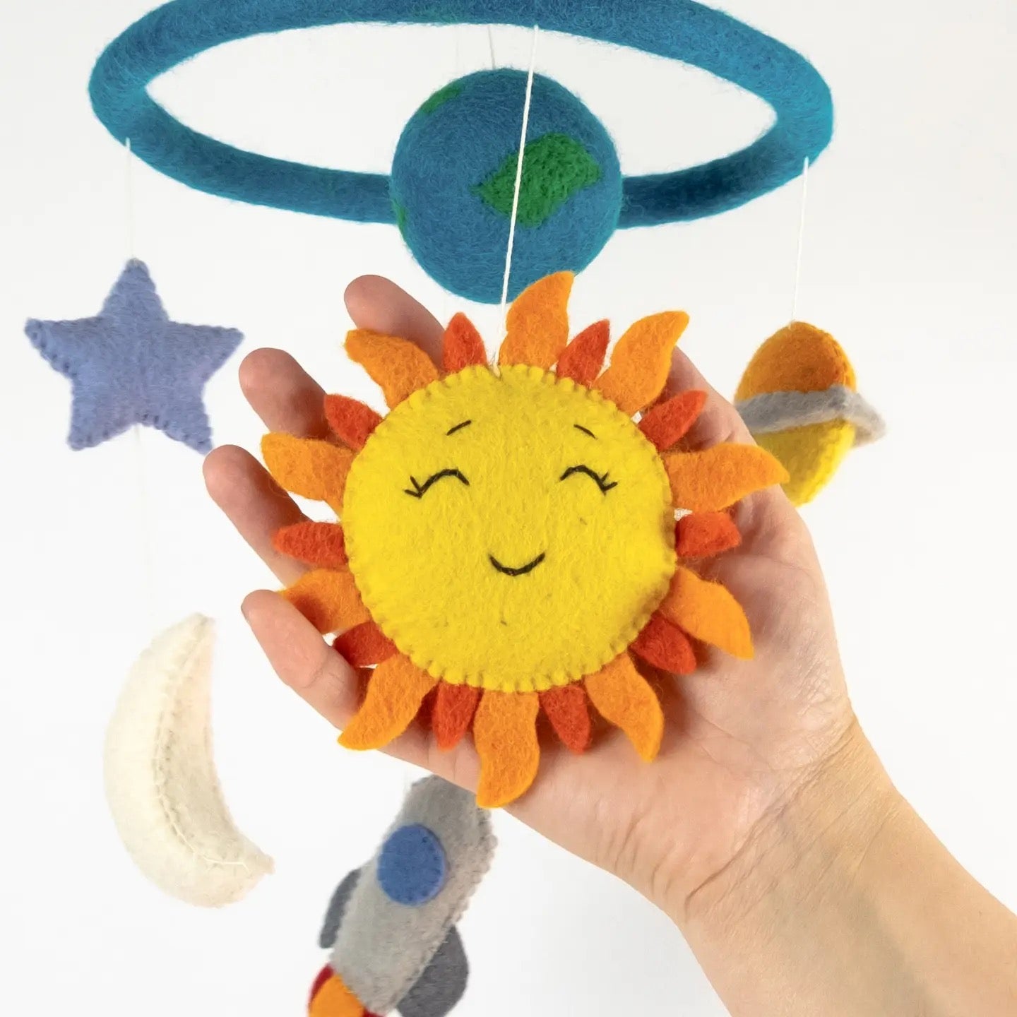 Hand holding a felt sun toy with a star and moon in the background