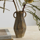 Decorative vase with ribbed texture and two handles on a wooden surface with a light background