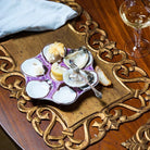 Oysters on a purple plate with a decorative gold tray and a glass of white wine.