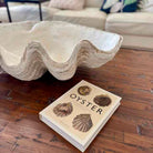 Large shell and book titled 'Oyster' on a wooden surface with a blurred background
