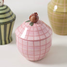 Pink ceramic jar with grid pattern and decorative lid on a white surface