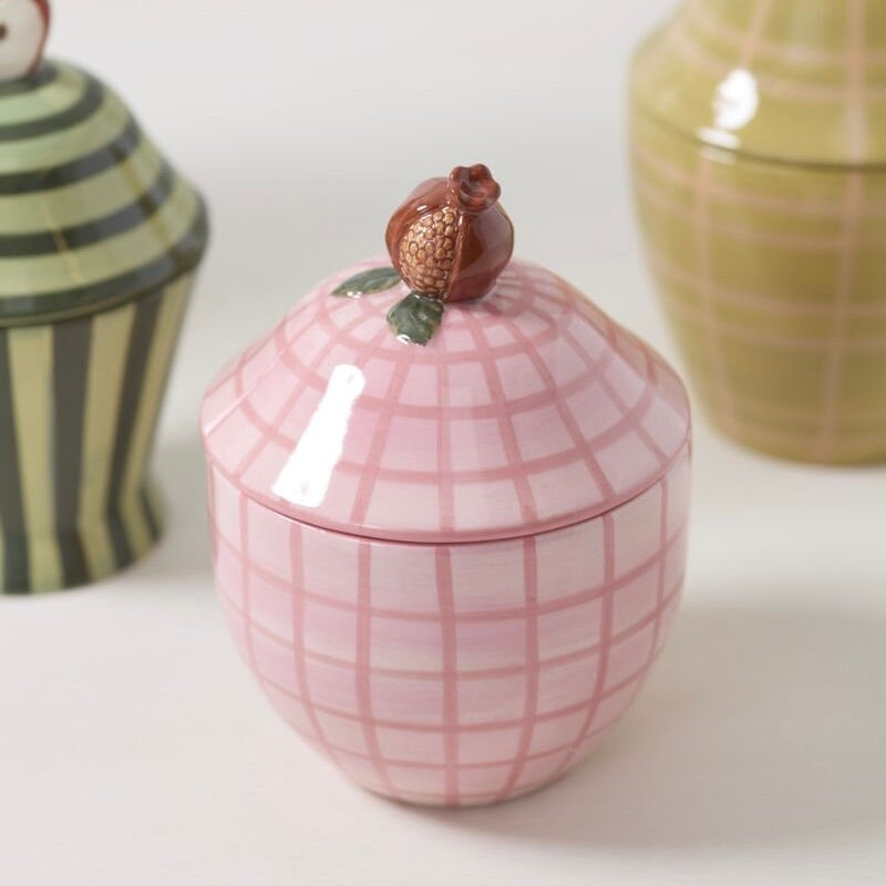 Pink ceramic jar with grid pattern and decorative lid on a white surface