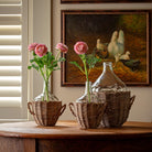Decorative vases with flowers on a wooden table in front of a painting of chickens.