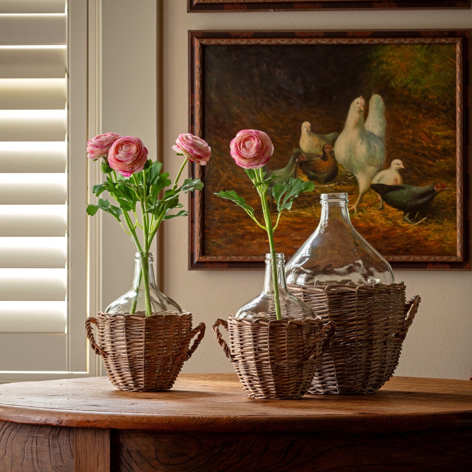 Decorative vases with flowers on a wooden table in front of a painting of chickens.