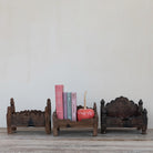 Wooden bookends with books and a decorative item on a wooden surface against a light gray wall.