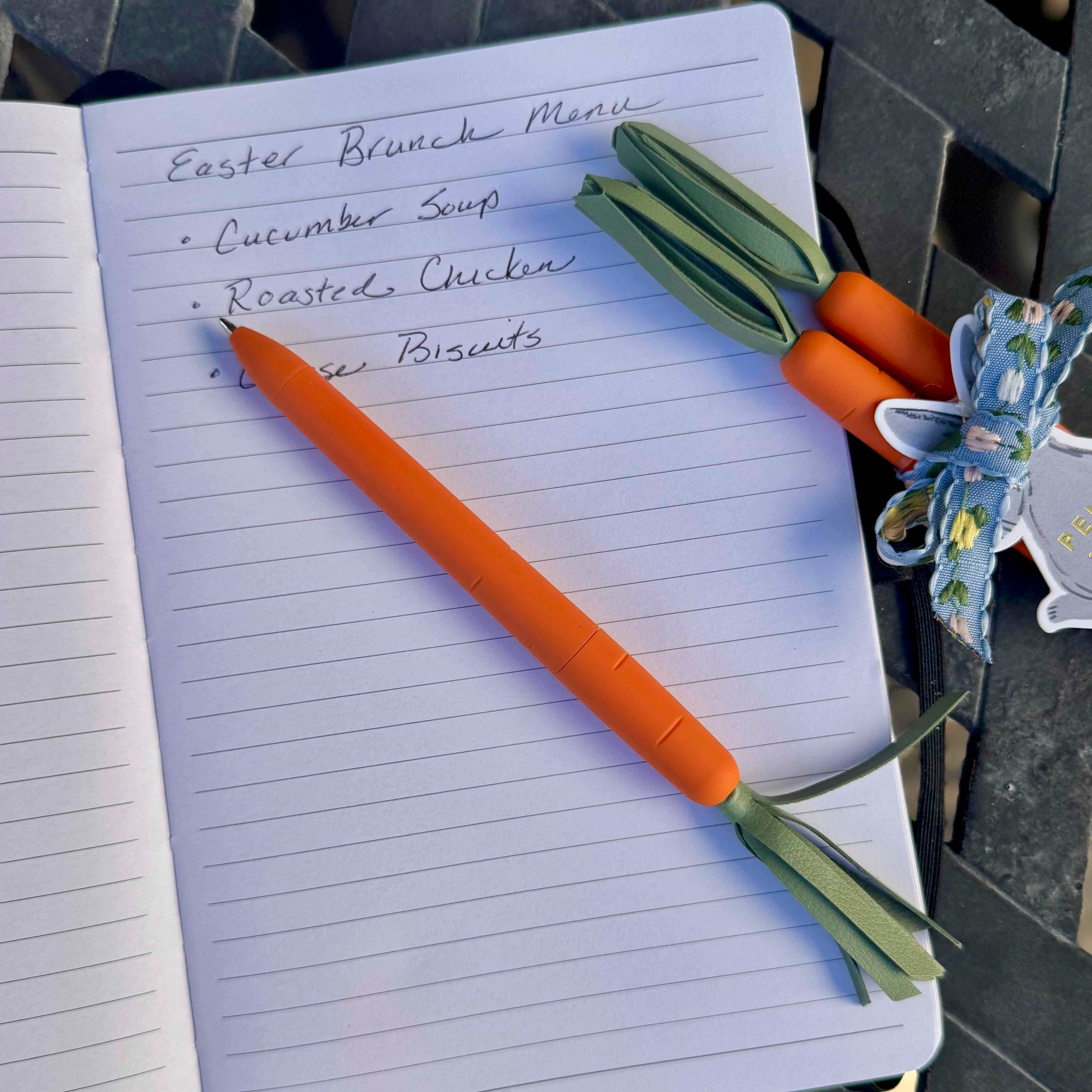 Notebook with Easter brunch menu and carrot-shaped pen on a table