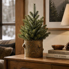 A small artificial evergreen tree in a rustic tree-trunk planter, styled on a wooden console table in a cozy living room setting.