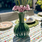 Green vase with pink flowers on a table with a floral tablecloth