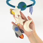 Hand holding a colorful baby mobile with stars, planets, and rockets against a white background