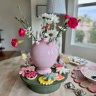 Pink vase with flowers on a table with decorative cookies and plates.