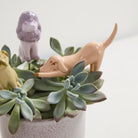 Decorative planter with succulents and small ceramic dogs on a white background
