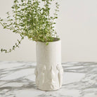 Cylindrical ceramic vase with textured surface holding a plant on a marble surface.