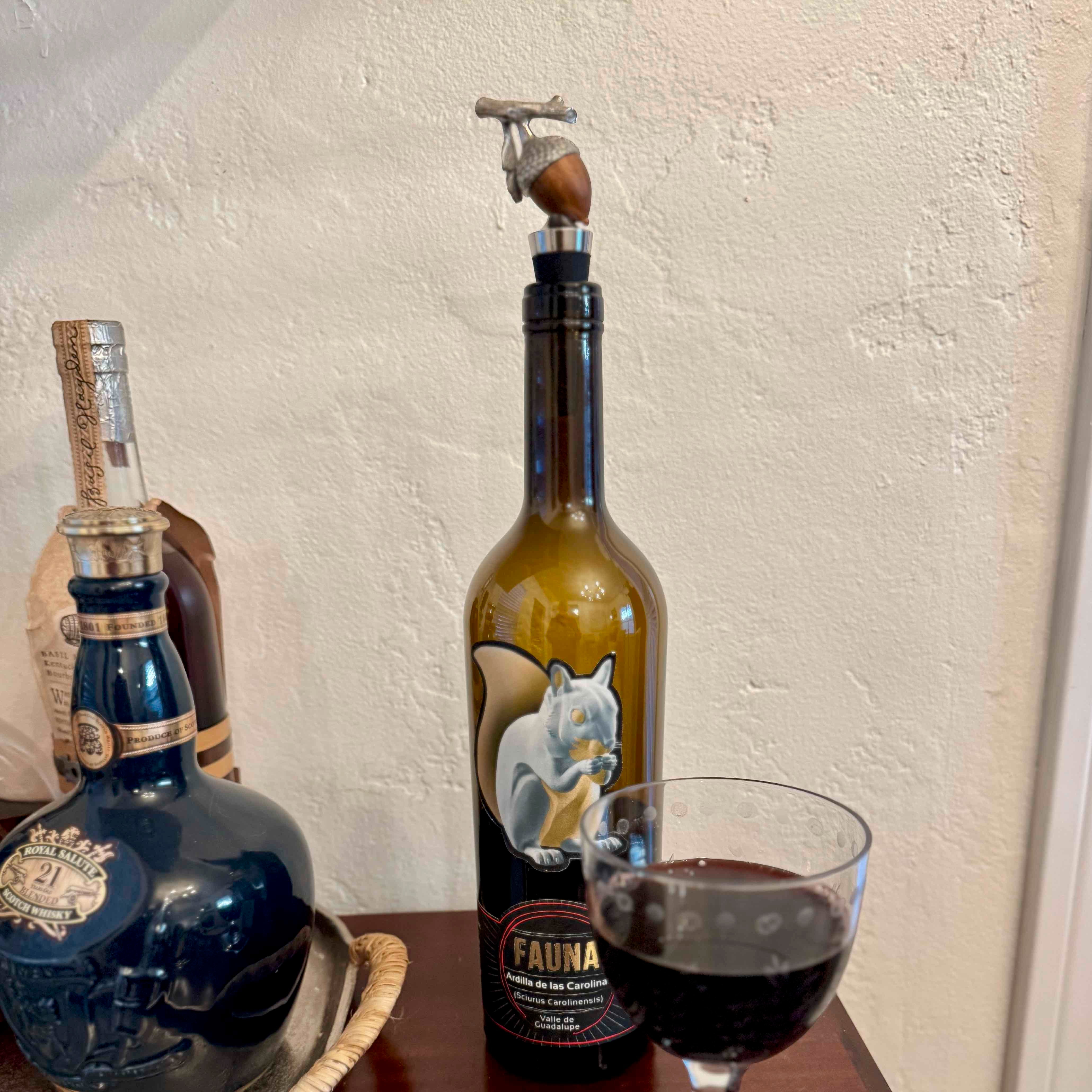 Bottle of Fauna wine with a pump, a glass of red wine, and another bottle in the background on a textured surface.