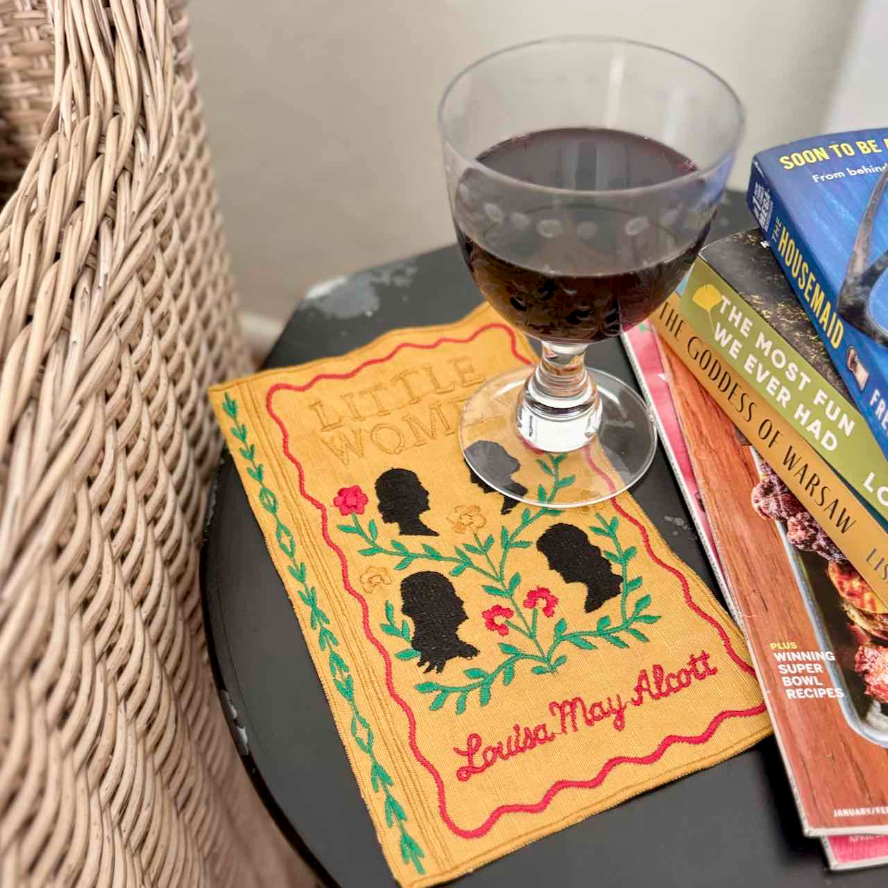 Glass of red wine on a book with decorative cover featuring silhouettes and floral elements.