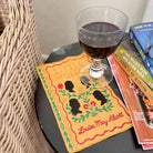 Glass of red wine on a book with decorative cover featuring silhouettes and floral elements.