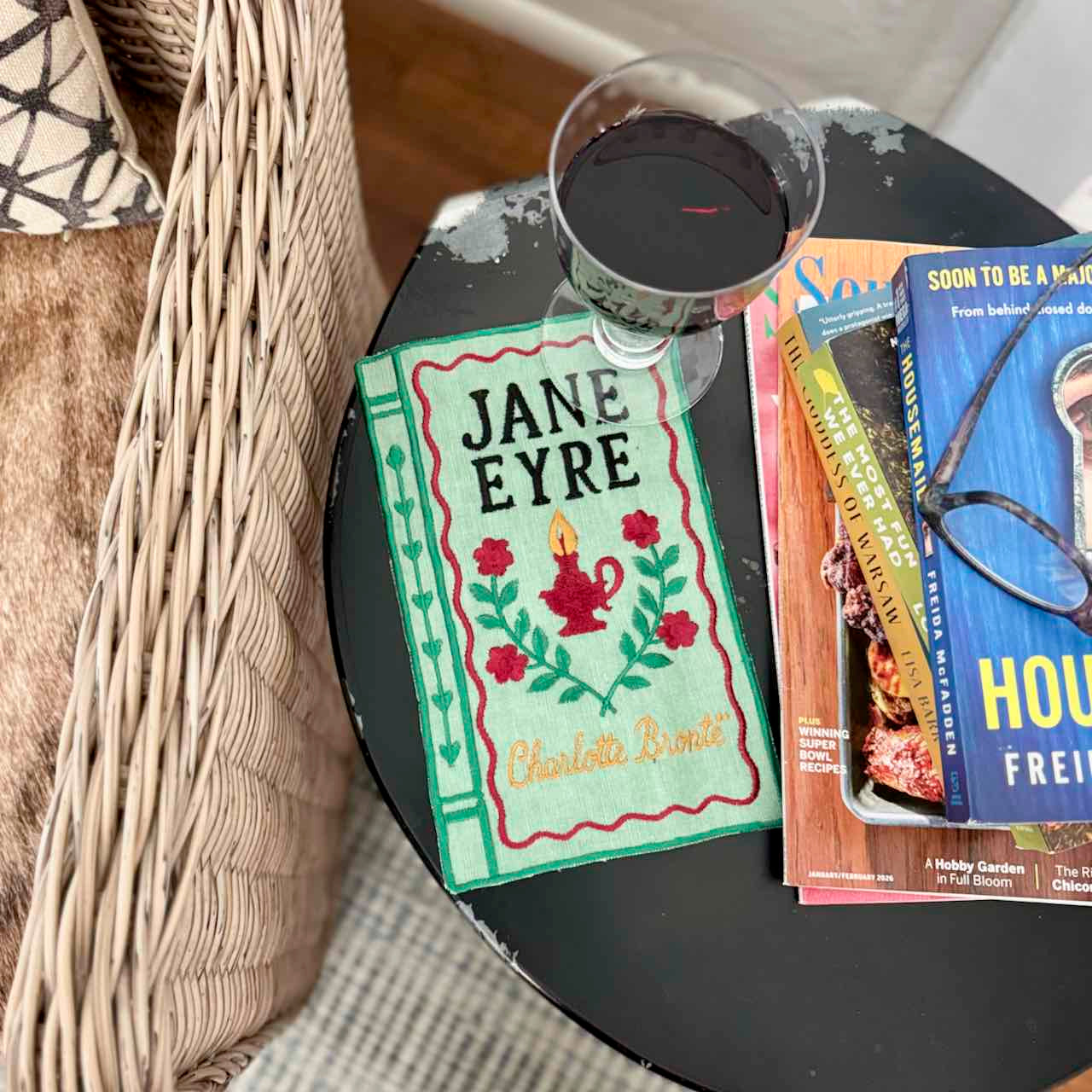 Book titled 'Jane Eyre' next to a glass of red wine on a table.