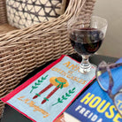 Glass of red wine on a decorative mat with a book and sunglasses in the background