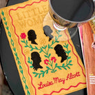 Book cover of 'Little Women' by Louisa May Alcott with a silhouette design and a cup on top.