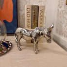 Silver donkey figurine on a surface with books in the background
