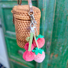 Woven bag with strawberry-shaped keychain against a green metal background