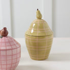 Two ceramic jars, one pink with a grid pattern and one green with a plaid pattern, on a white background.