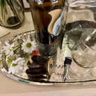 Bottle of wine, corkscrew, and daisies on a silver tray with a blurred background.